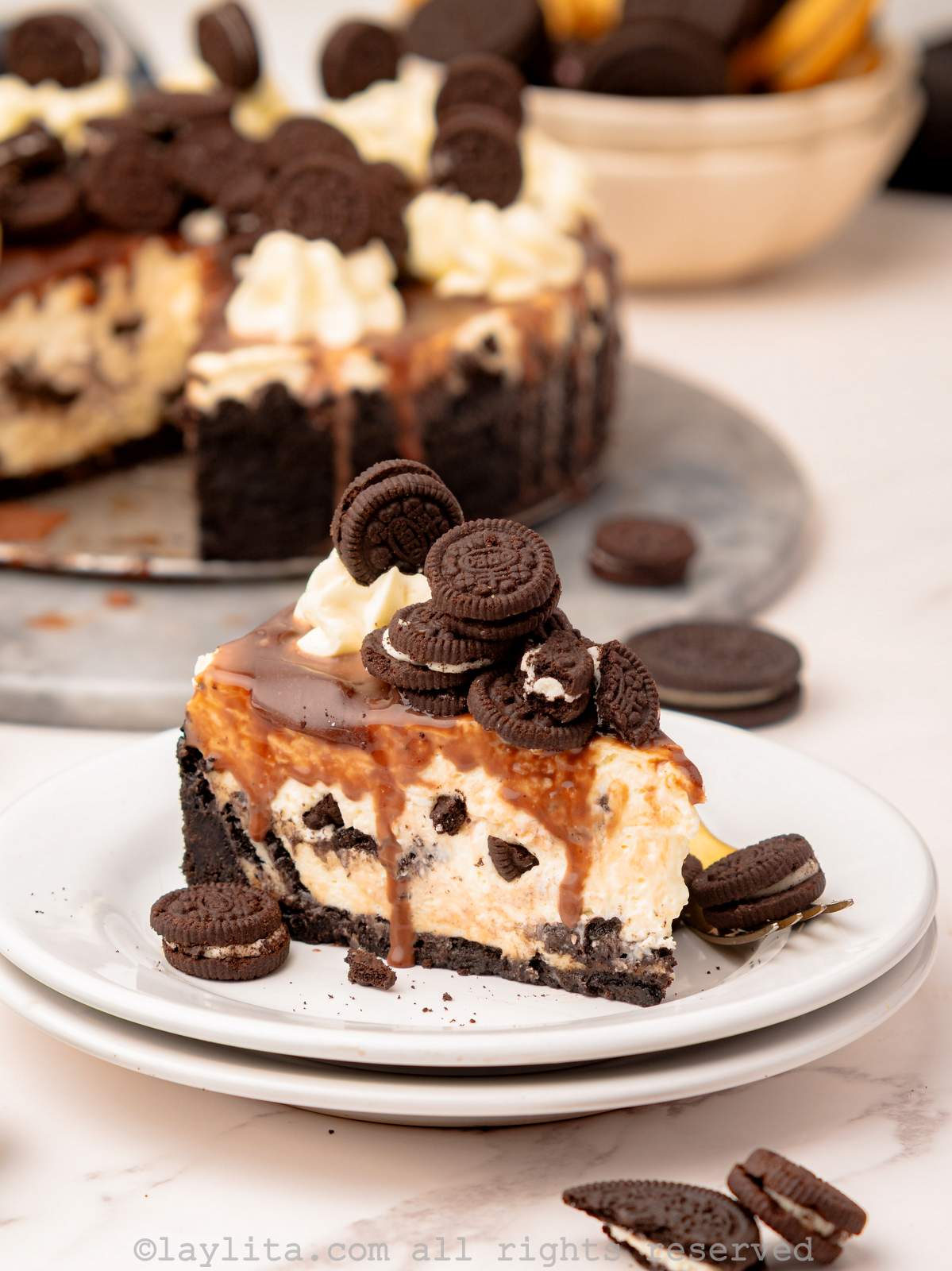 Slice of no bake oreo cheesecake on a plate with the rest of the cheesecake in the background.