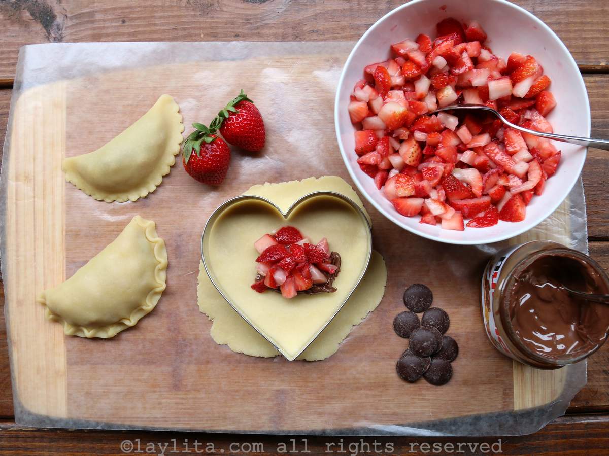 Filling the empanada dough with strawberries and chocolate on a wooden board
