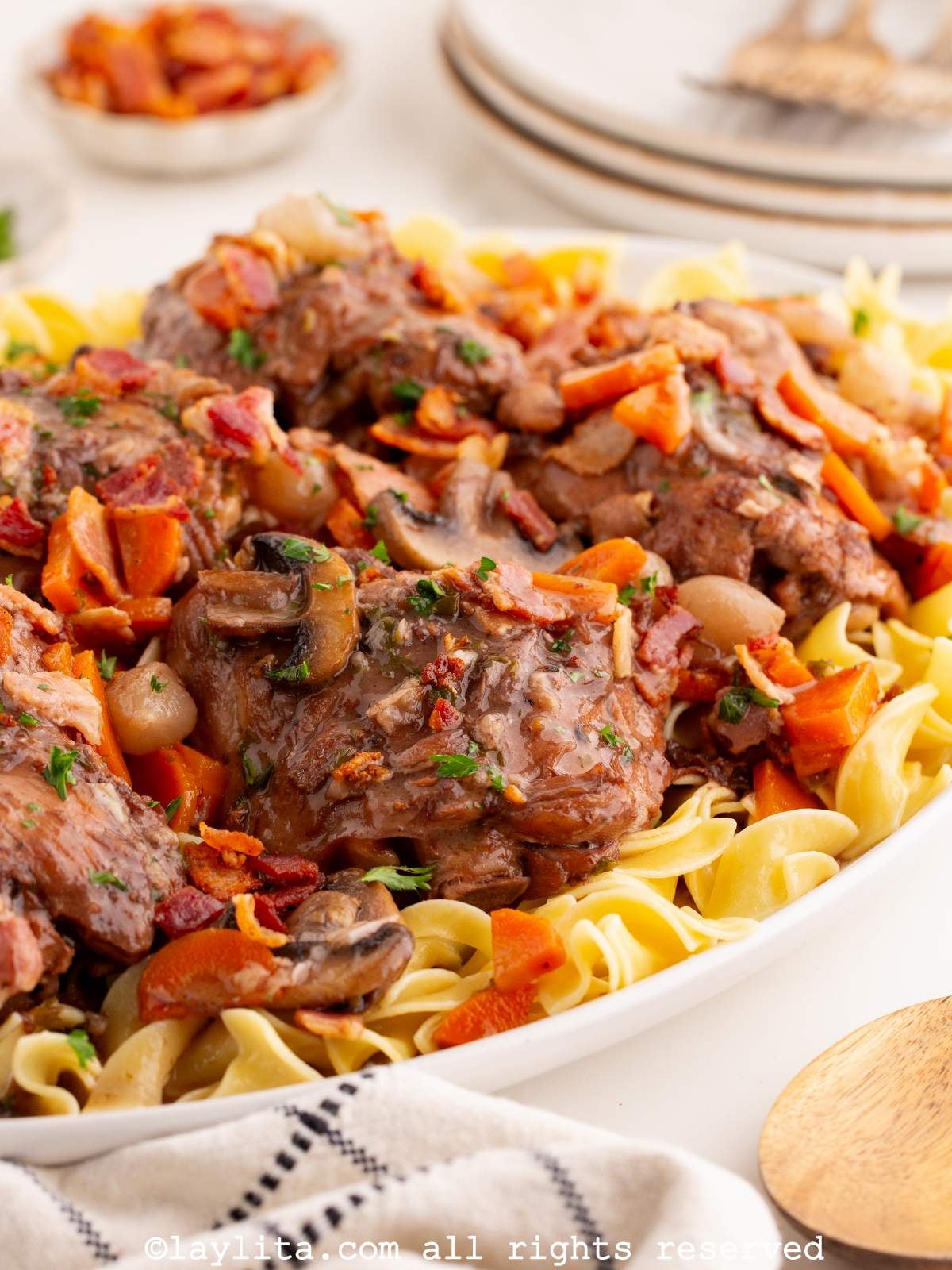 Side view of a platter filled with chicken thighs in red wine sauce served over egg noodles