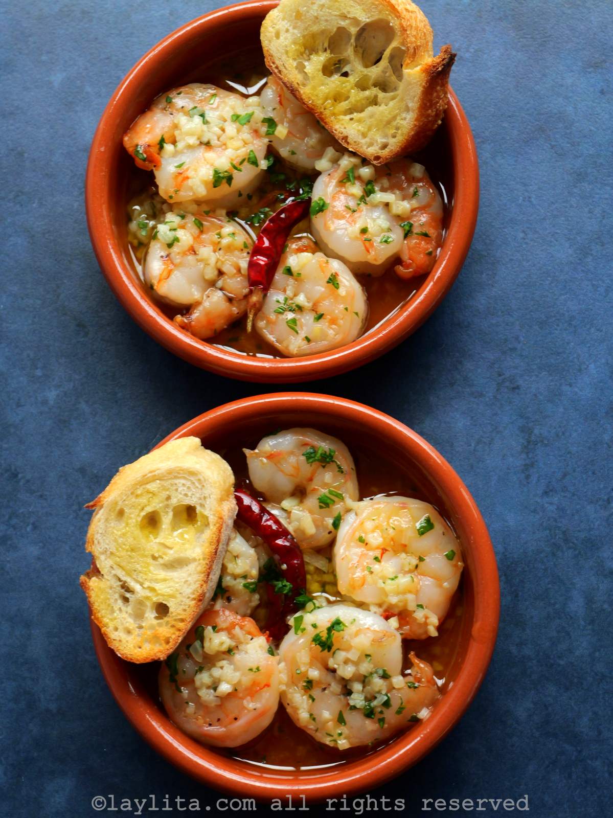 Overhead shot of two bowls filled with Spanish gambas al ajillo style garlic shrimp, served with slices of bread