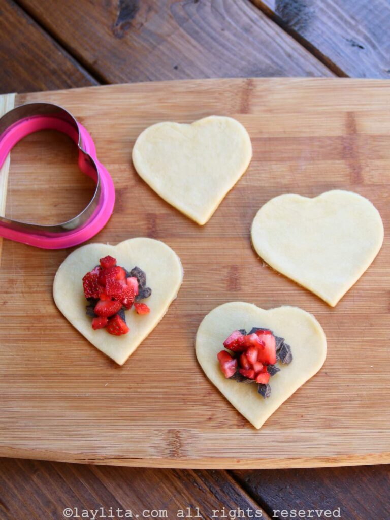 Filling the heart shaped empanada dough with strawberries and chocolate on a wooden board