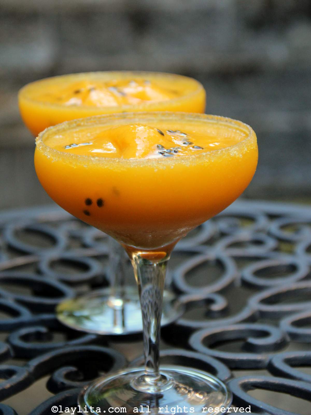 Two coupe glasses filled with mango passion fruit margaritas on a black cast iron table