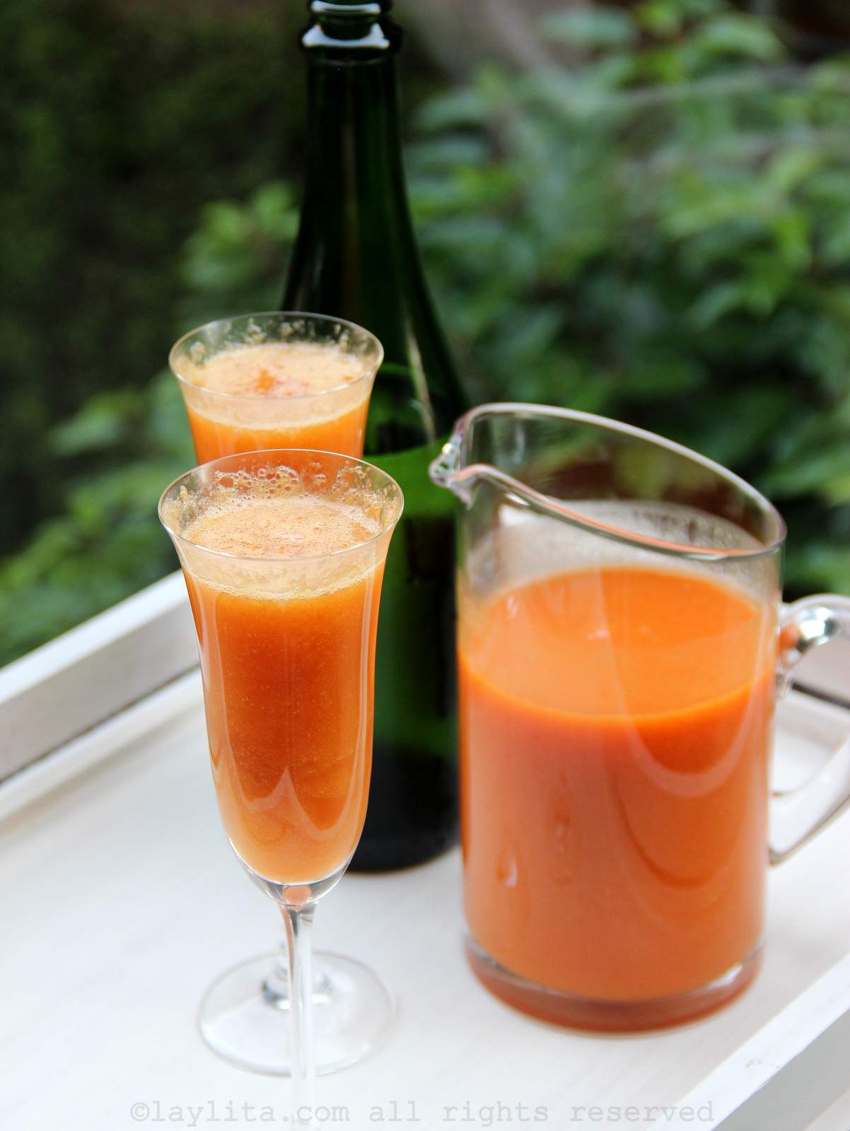 Peach bellini cocktails in two champagne glasses with a pitcher and a bottle of sparkling wine in the background