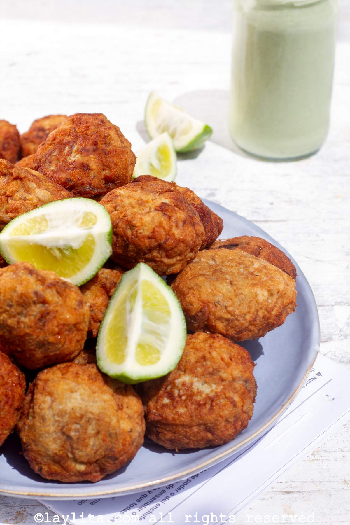 Salt Cod Buñuelos on a plate with lime wedges on top and a green herb aioli in the background