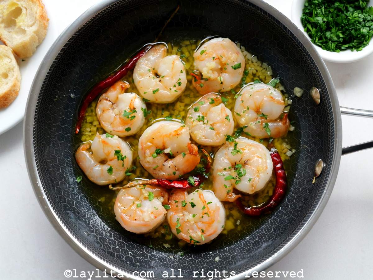 Small black skillet filled with cooked garlic shrimp with chopped parsley and bread slices in the background