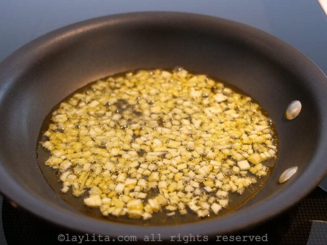 Diced garlic cooking in olive oil in a small black skillet