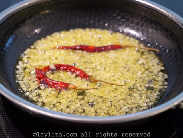 Diced garlic and three whole dry chili peppers cooking in olive oil in a small black skillet