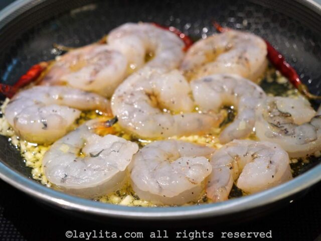 Raw shrimp being added to a skillet with garlic and olive oil