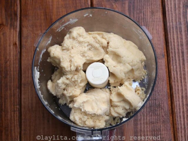 Clumpy dough in a food processor on top of a wooden table