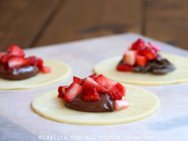 Filling the empanada dough with strawberries and Nutella on a wooden board