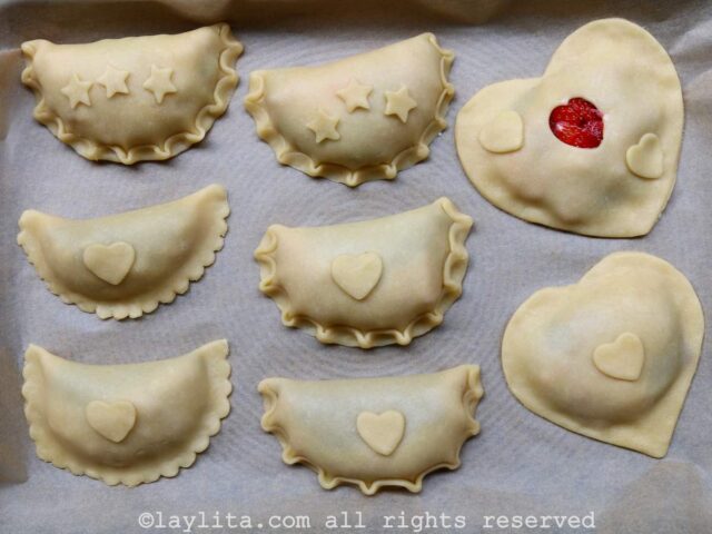A tray filled with unbaked empanadas, some in heart shapes and other decorated with mini hearts