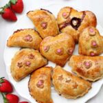 A plate of Valentines Day sweet empanadas on a white plate with fresh strawberries on the side