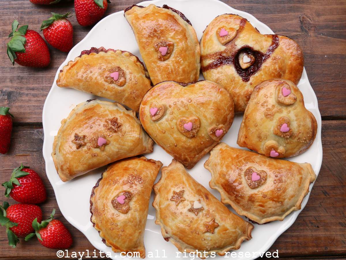 Chocolate strawberry empanadas, some in heart forms, on a white plate with fresh strawberries on the side