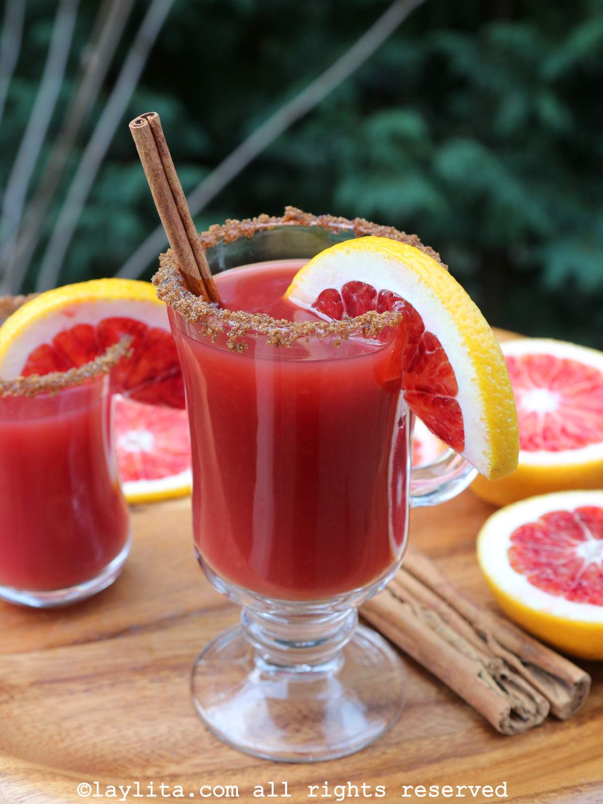 A glass full of Warm spiced blood orange canelazo cocktail garnished with a cinnamon stick and a slice of blood orange