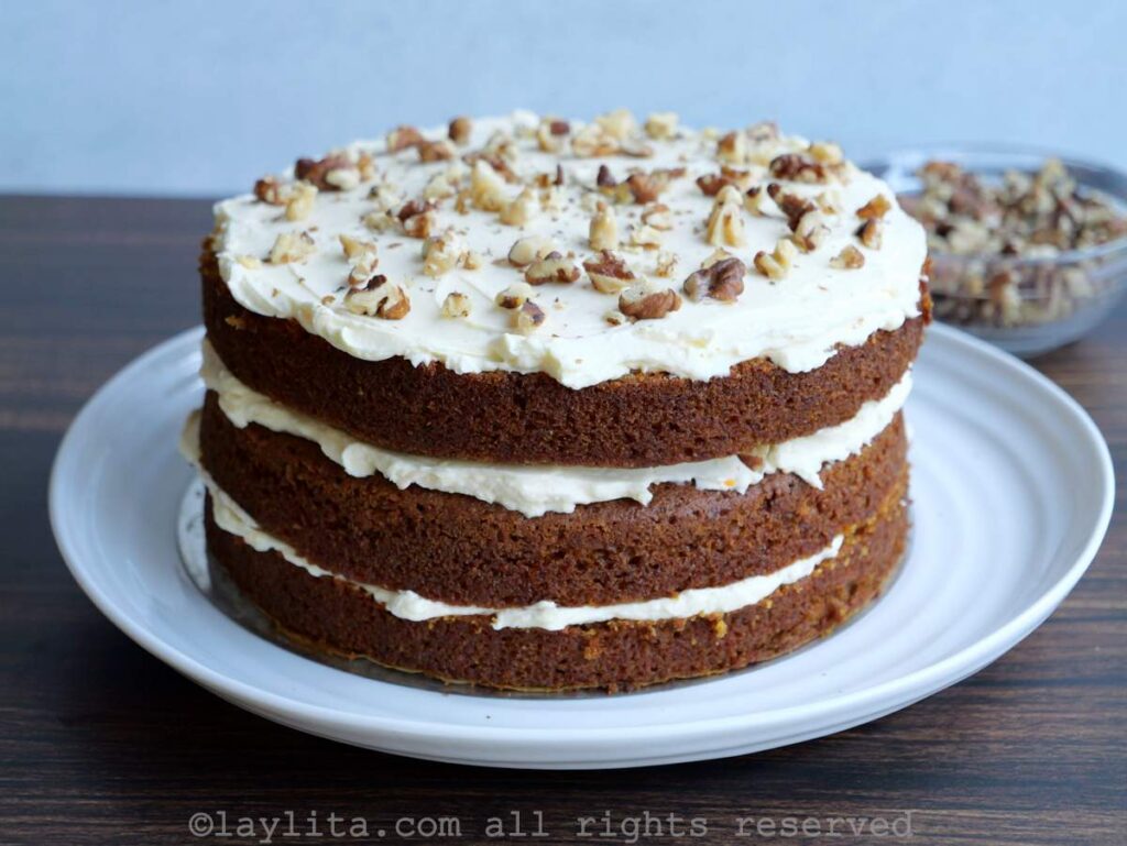 A naked carrot cake with cream cheese frosting and nuts on top
