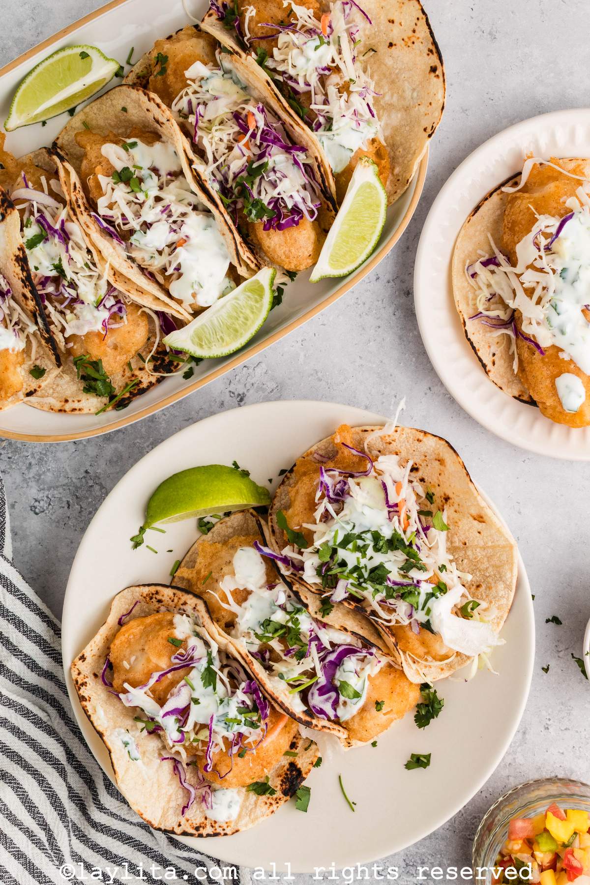 Overhead view of several plates of fish tacos, with lime wedges and a striped napkin on the side