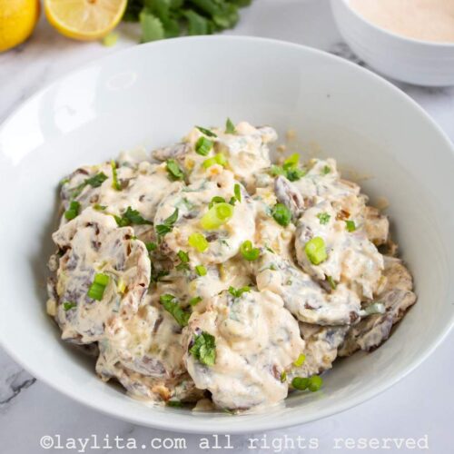 Side view of smashed potato salad on a plate with lemons and herbs in the background.