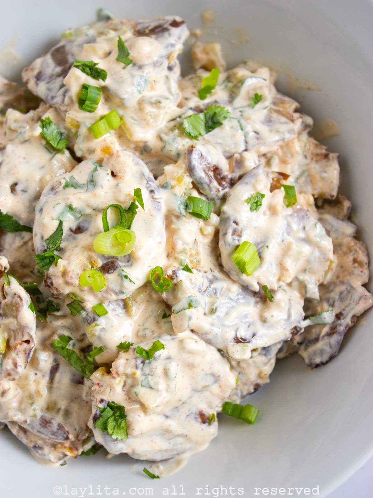 Closeup of crispy smashed potato salad in a white bowl with green onions on top