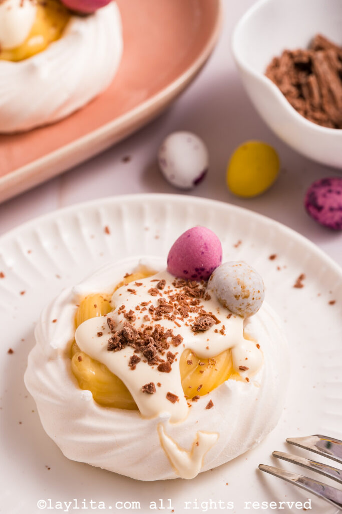 A meringue nest filled with lemon custard and topped with cream and chocolate shavings on a white plate