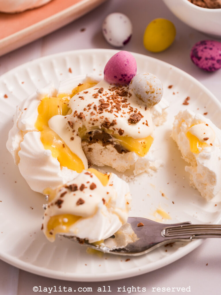 A meringue nest broken apart with a fork showing the lemon filling on a white plate