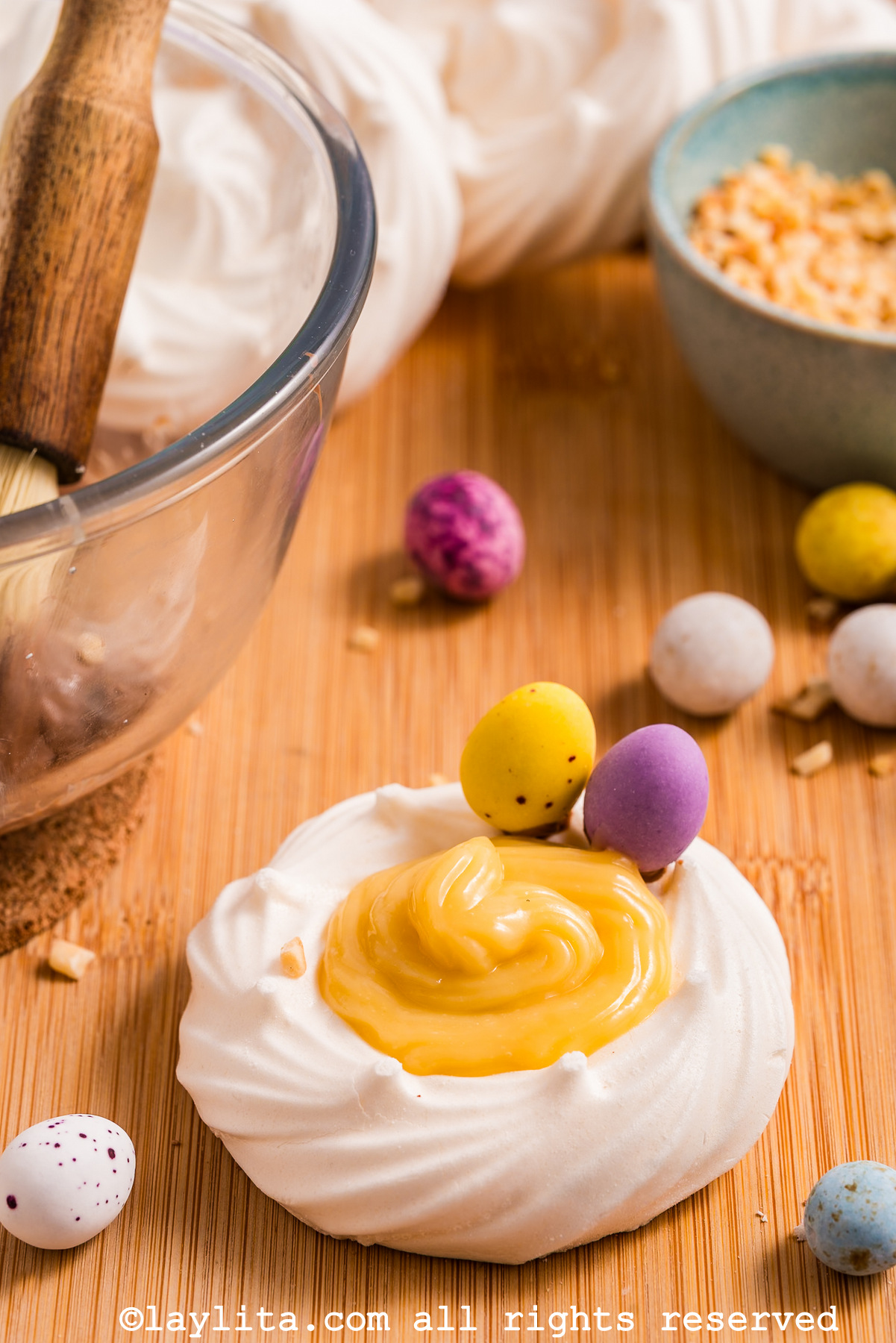 A meringue nest filled with lemon custard and decorated with two mini chocolate eggs, with more eggs in the background