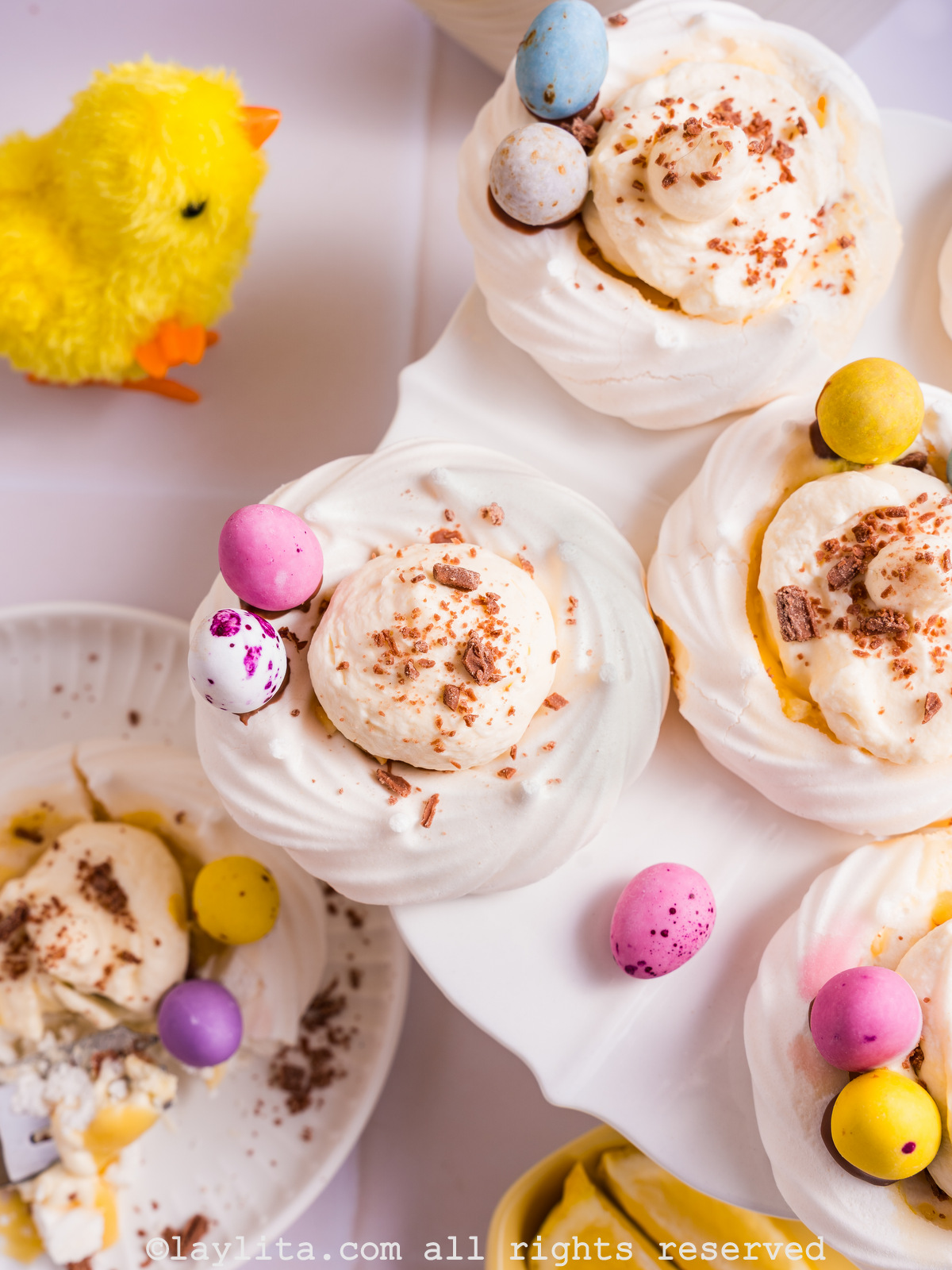 Overhead view of Easter Meringue Nests filled with Lemon Custard Cream filling and decorated with chocolate shavings and mini eggs, with a decorative easter duck on the side
