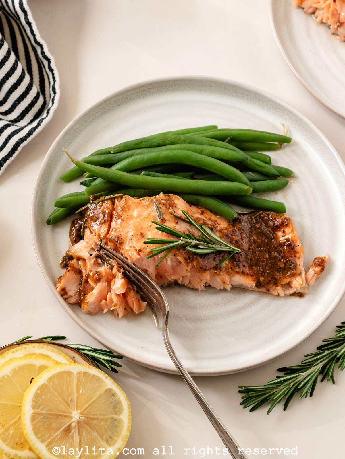 Overhead view of roasted salmon and green beans on a white plate, with some lemon slices on the side
