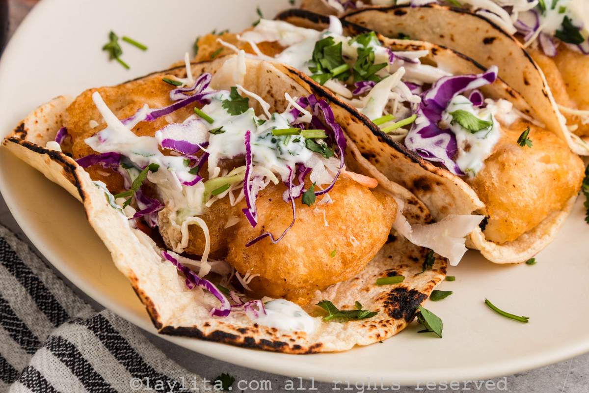 Two cod fish tacos topped with cabbage slaw and Mexican crema on a white plate