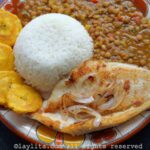Fish a la plancha on a plate next to rice, plantains, and lentils.