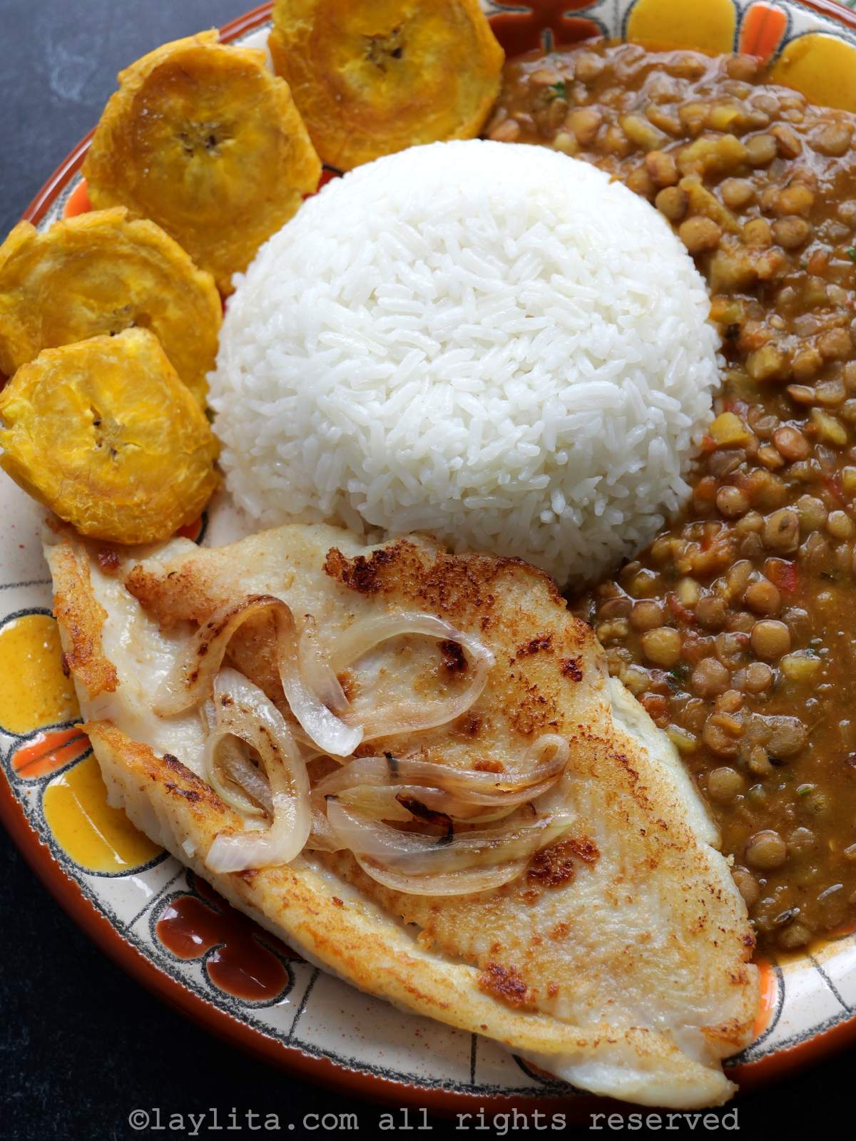 Overhead view of fish or pescado a la plancha on a plate next to rice, lentils and patacones
