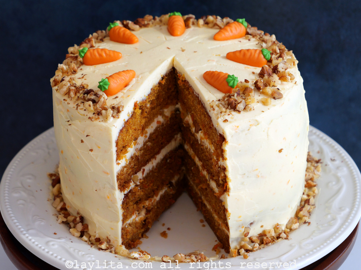 Four layer carrot cake with cream cheese frosting on a white platter, with a slice missing to show the layers inside the cake