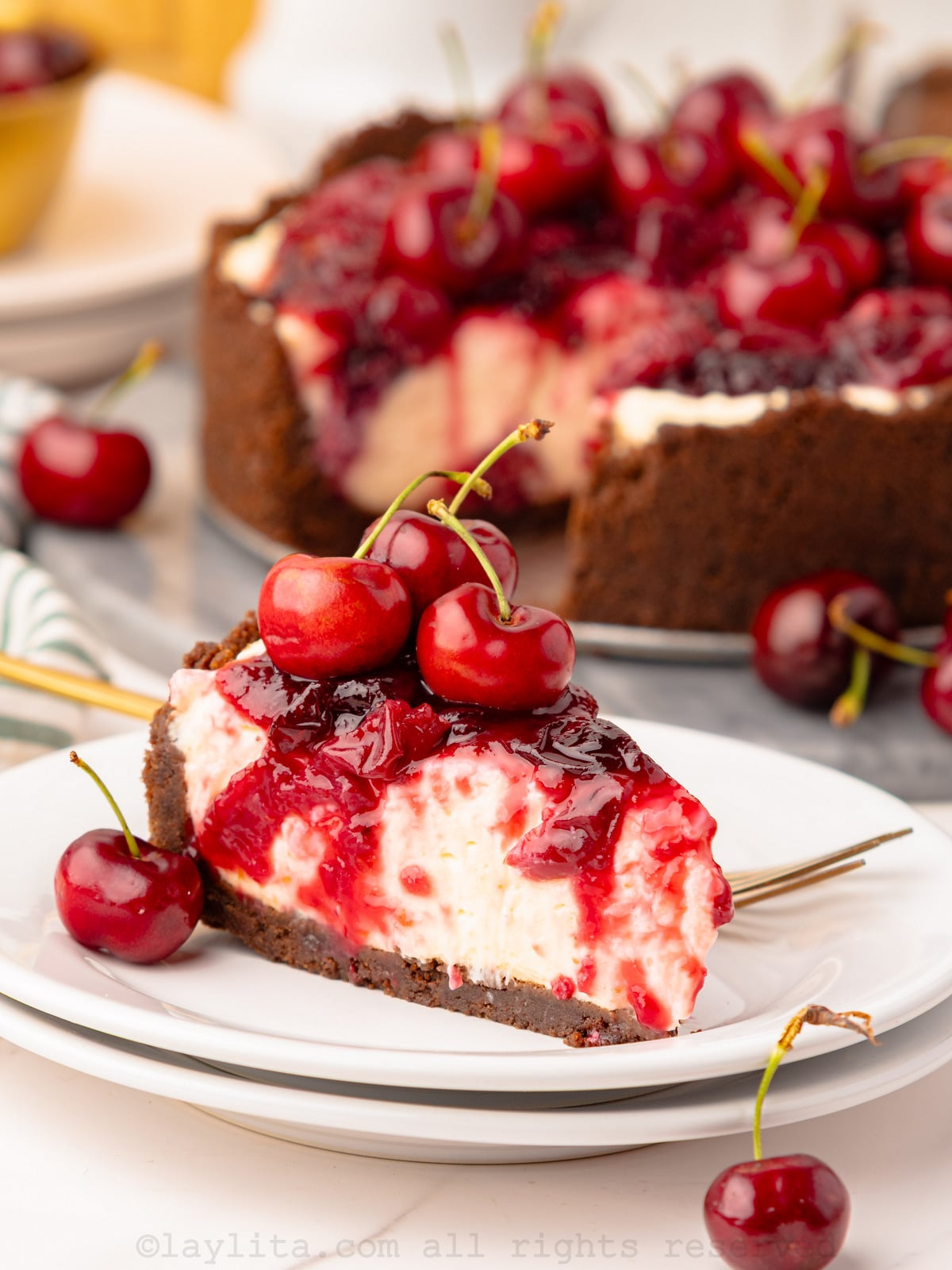Slice of no bake cherry cheesecake on a plate with the rest of the cheesecake behind it.