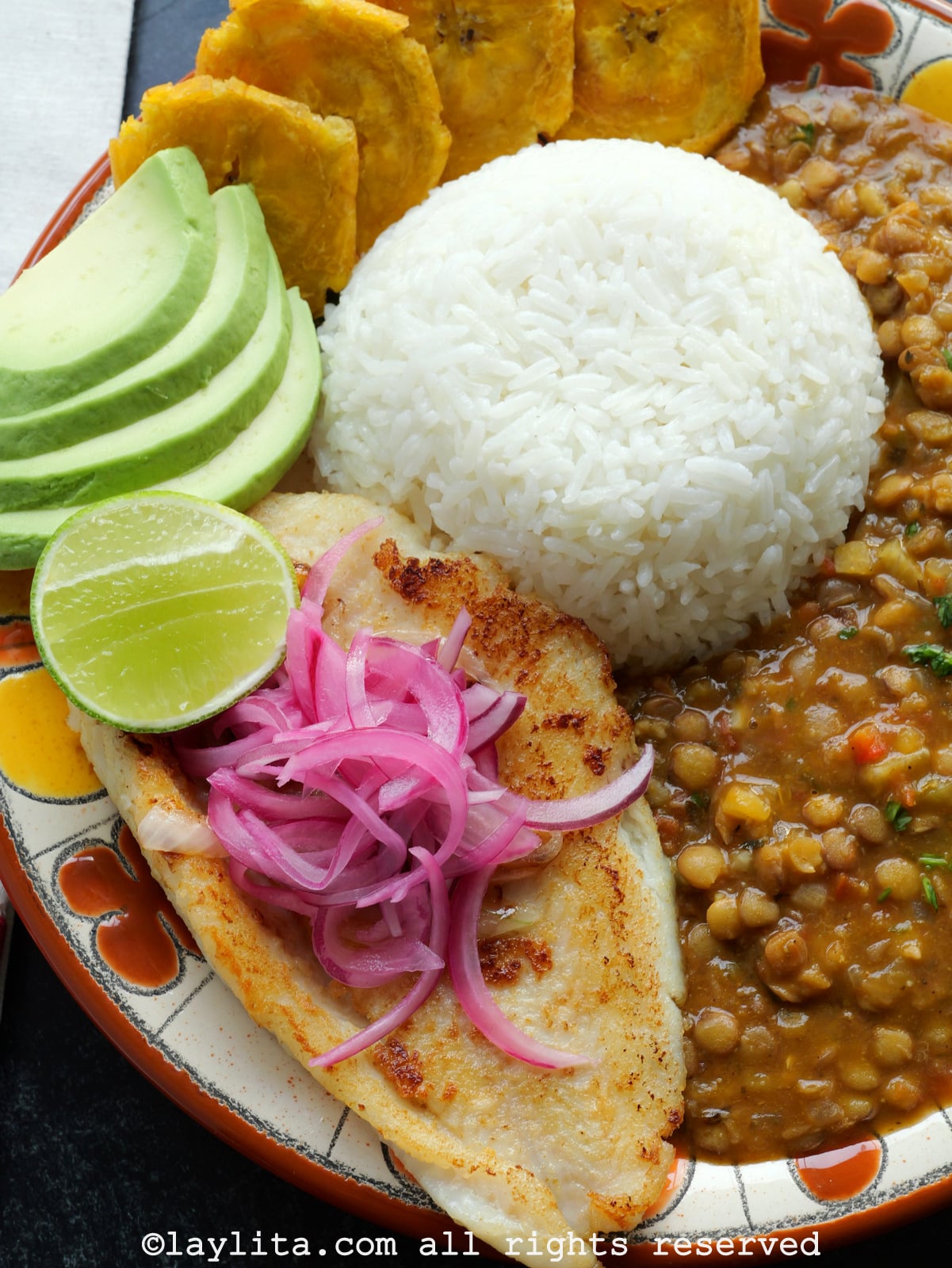 Close up of pescado a la plancha style fish on a plate with rice and lentils, with red onions on top of the fish.