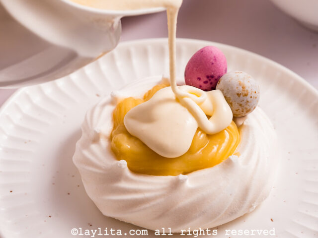 Thick cream being pour on top of a lemon custard filled meringue nest