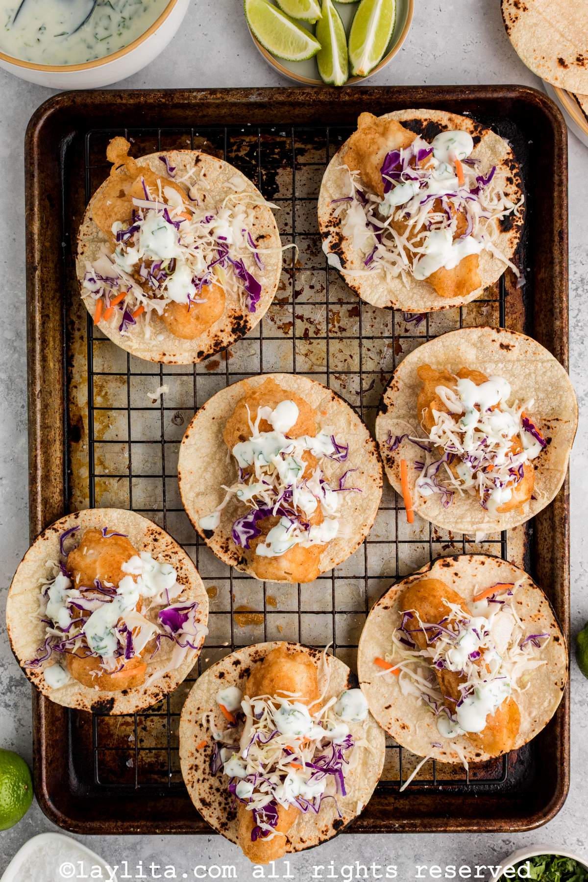 Overhead view of a baking rack full of fish tacos being assembled on a wire rack