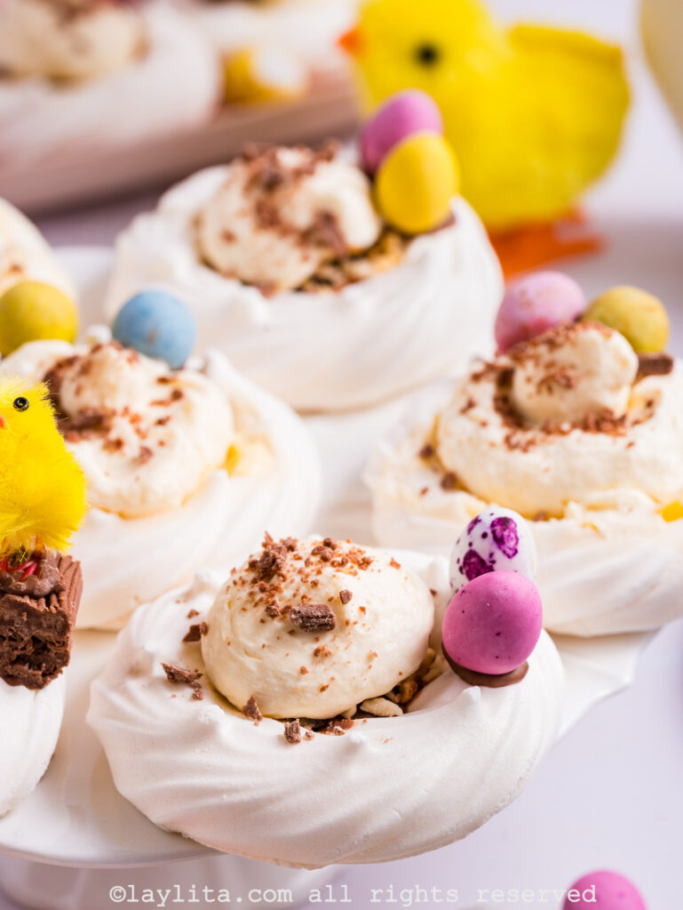 Several meringue nests filled with lemon custard cream and topped with chocolate shavings, with mini eggs on the side