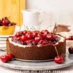 A no bake cherry cheesecake with a chocolate cookie crust on a marble platter with a few cherries on side and more in the backgroun