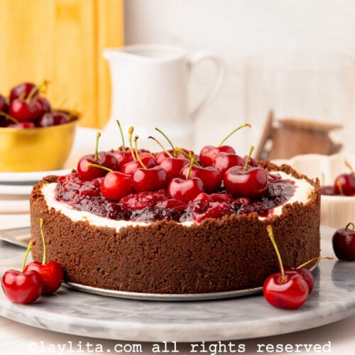 A no bake cherry cheesecake with a chocolate cookie crust on a marble platter with a few cherries on side and more in the backgroun