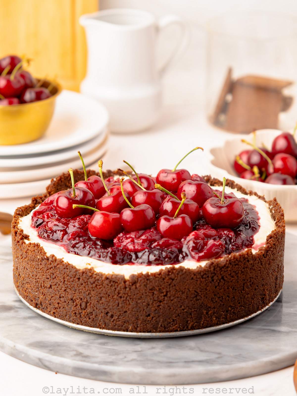 Vertical view of a cherry cheesecake topped with cherry compote and fresh cherries on a gray marble serving platter