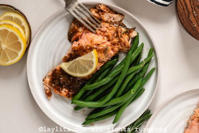 Overhead view of a white plate with a piece of roasted salmon, steamed green beans and a lemon slice