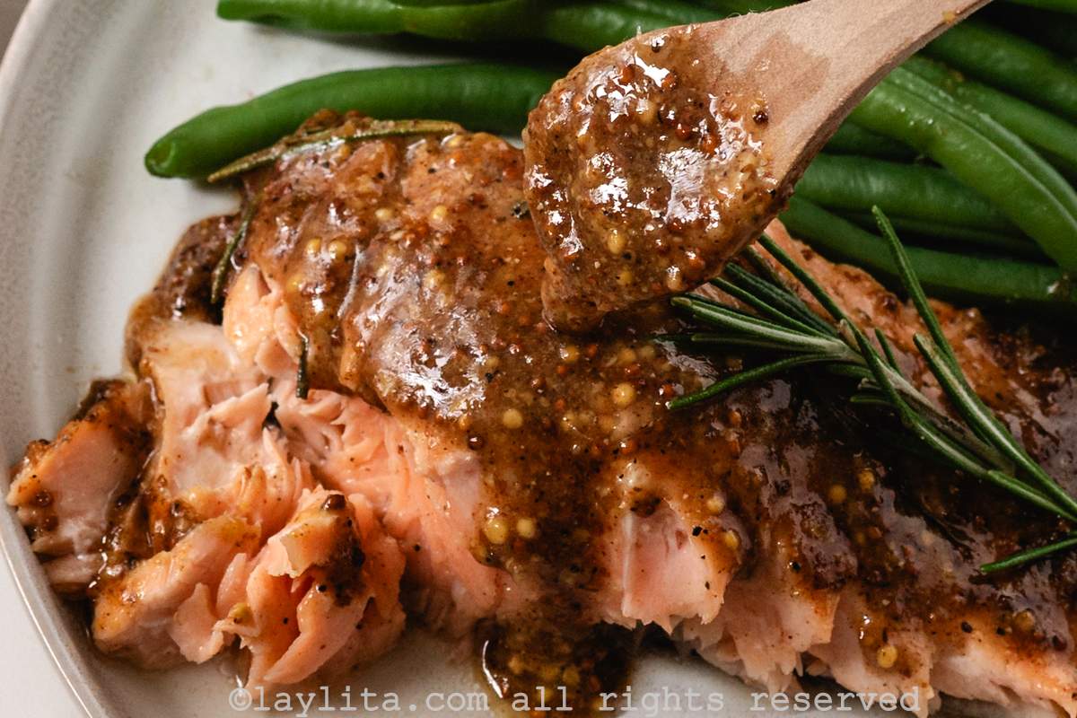 A spoon adding mustard maple glaze to a piece of baked salmon