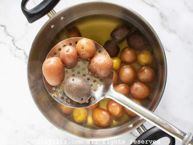 A pot full of boiled baby potatoes with a slotted spoon showing five of them