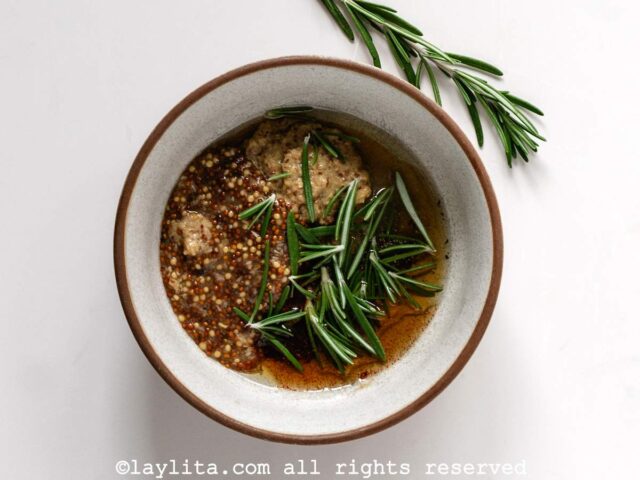A small bowl with maple syrup, mustard, olive oil, spices, and rosemary