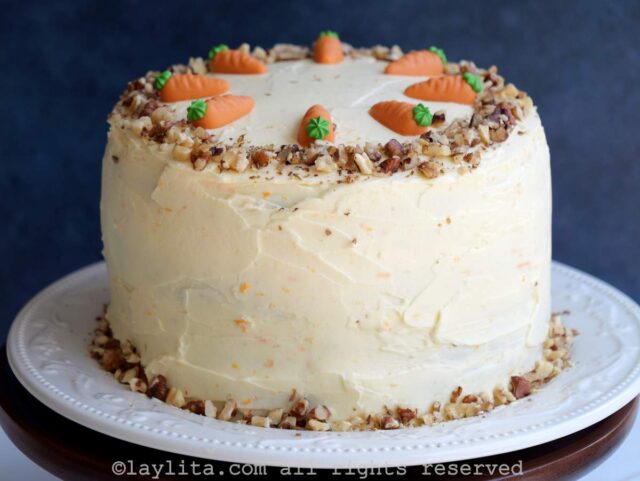 Carrot cake decorated with frosting and crushed nuts on a white platter