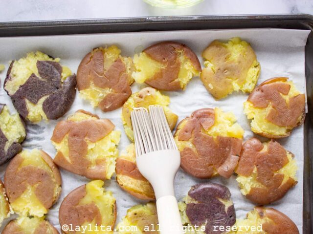 Closeup of a baking sheet lined with parchment paper with smashed potatoes on it