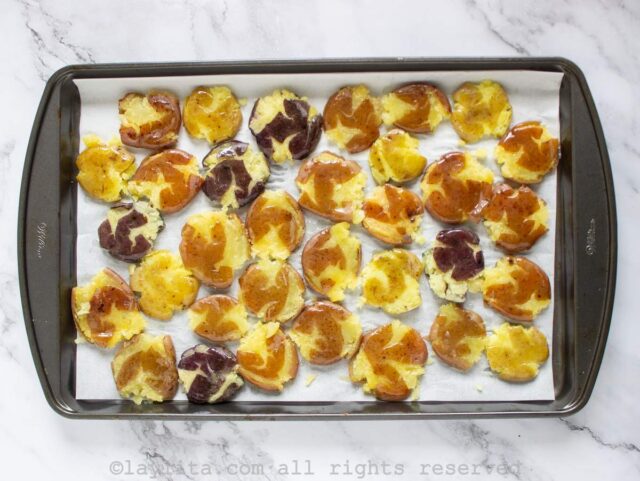Smashed potatoes on a baking sheet drizzled with olive oil