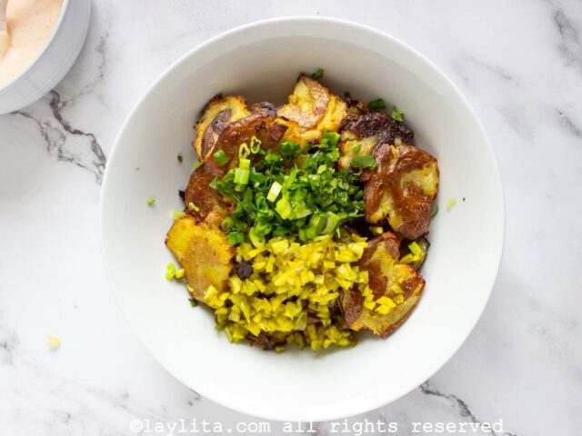Crispy potatoes with chopped onions, herbs and pickles in a bowl
