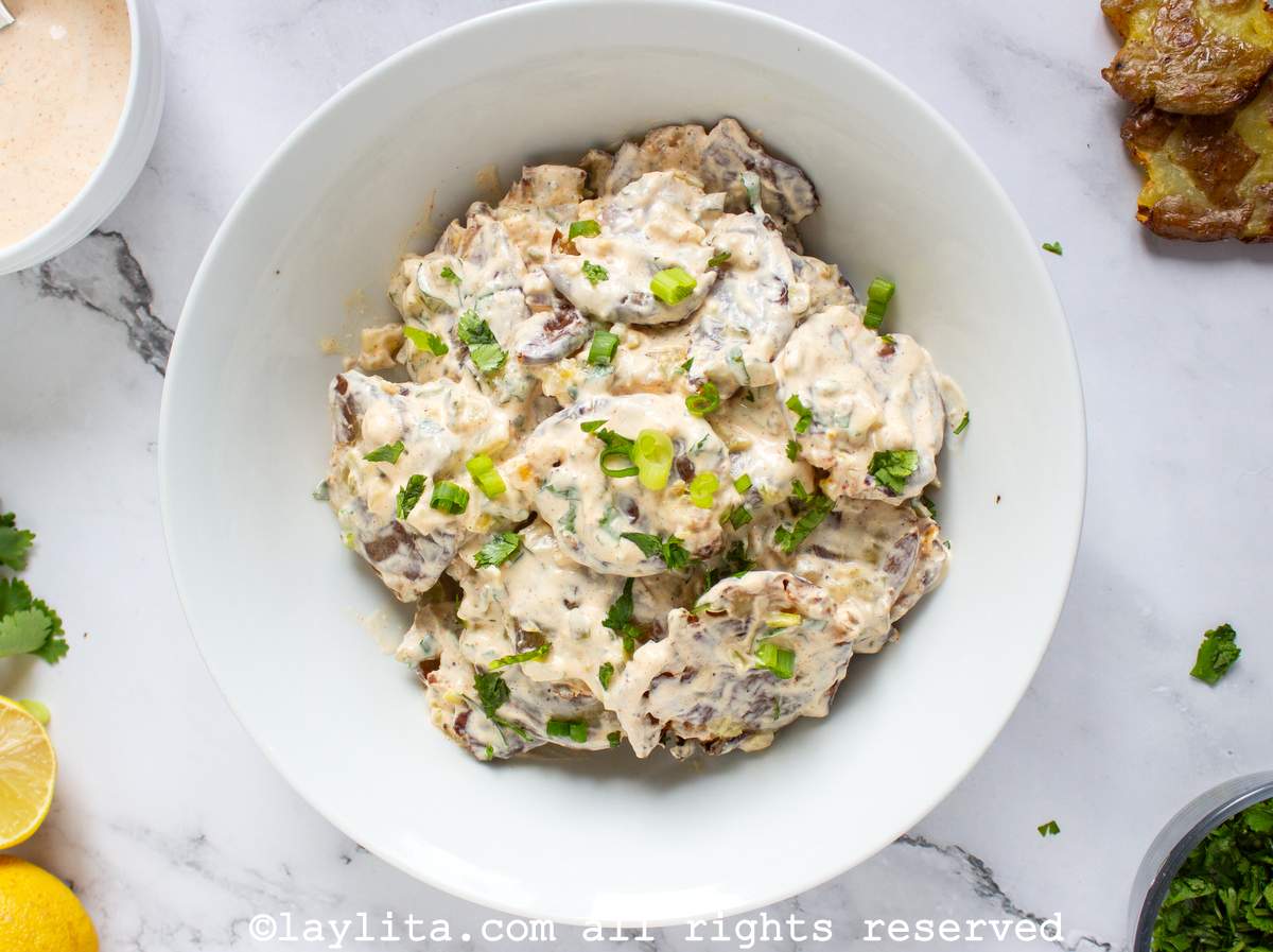 Overhead shot of crispy smashed potato salad in a bowl next to a small bowl of dressing, a half cut lemon and a couple of smashed potatoes