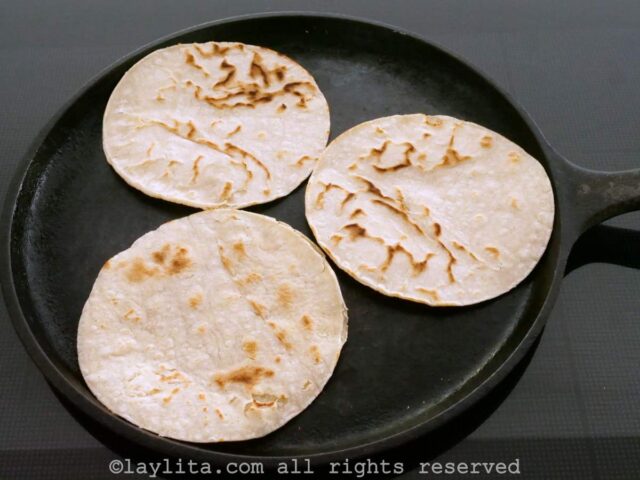 Three corn tortillas being warmed up on a griddle pan