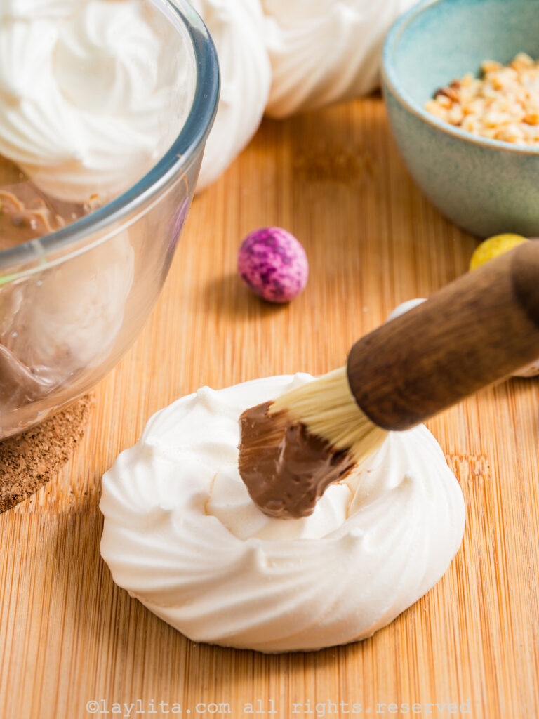 Melted chocolate being brushed on a meringue nest